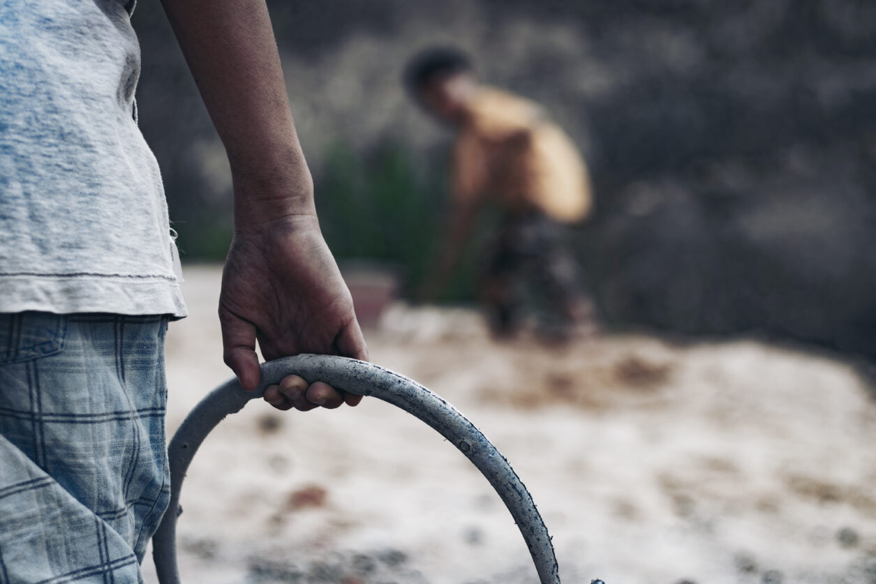 A child holds a bucket with another child in the distance.