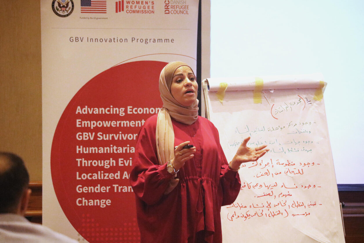 A woman in a red dress speaking about economic empowerment and gender-based violence.