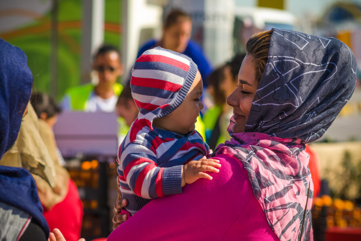 A woman in a pink shirt holds a baby wearing a striped sweater.