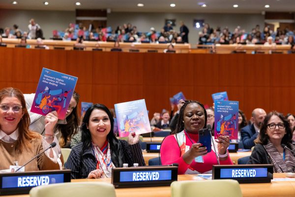 women sit in the UN chamber holding pamphlets about progress on gender equality